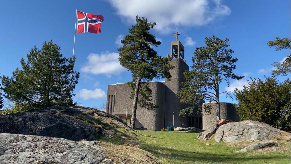 Foto av Grim kirke med flagg og blå himmel. 